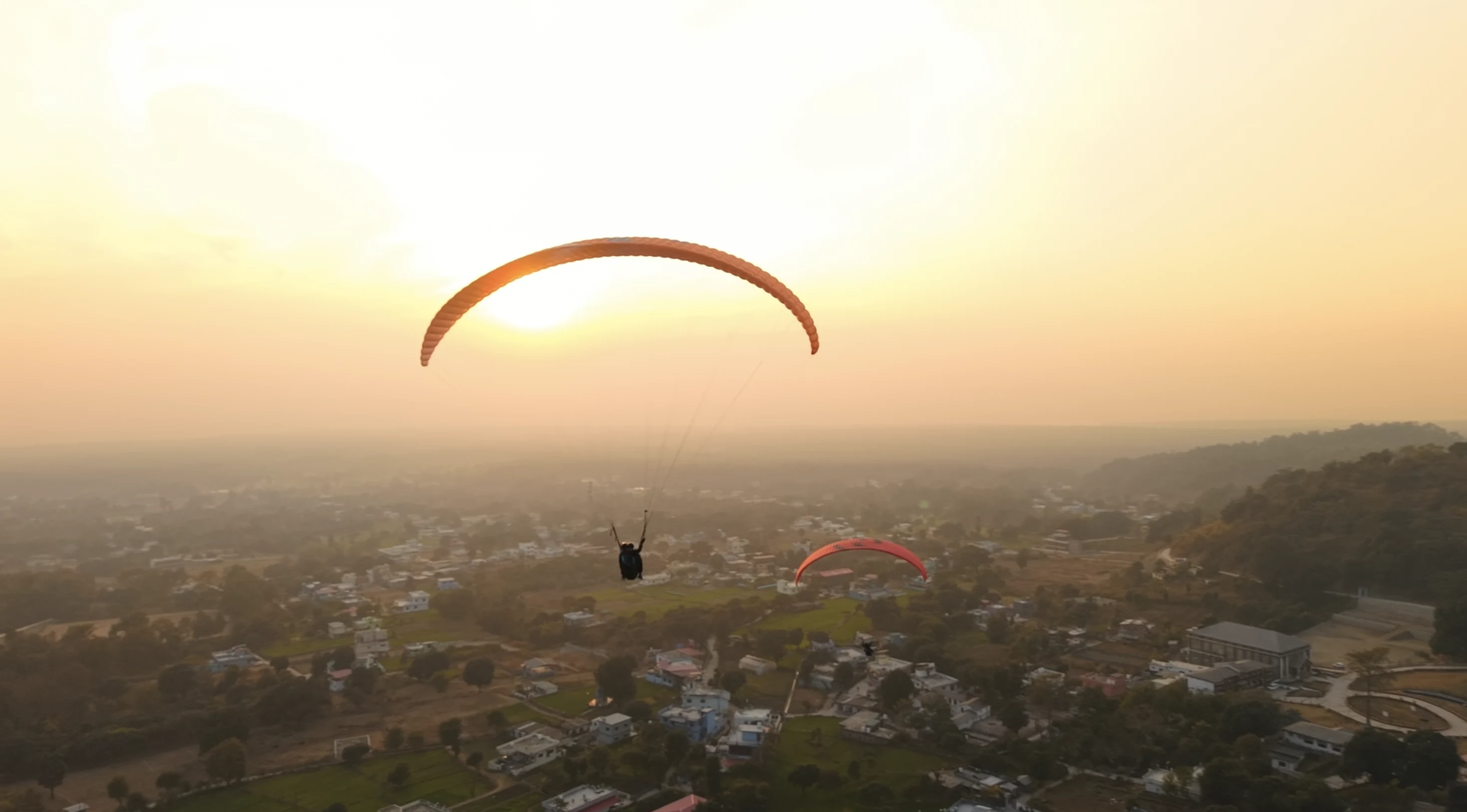 A person paragliding with a purple wing over the scenic turquoise waters of Tehri Lake surrounded by mountains in Uttarakhand, India.